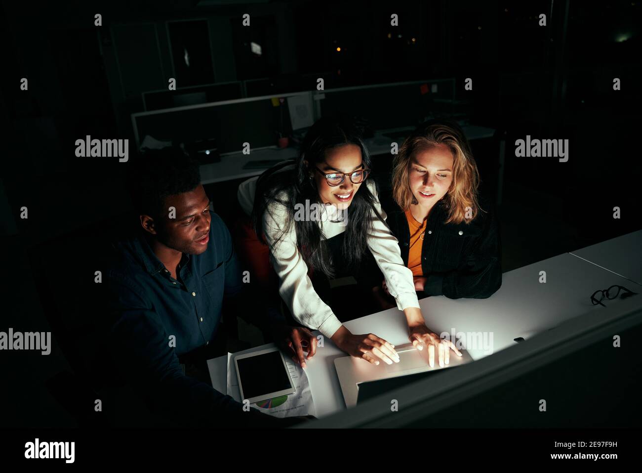 Une équipe professionnelle multiethnique qui a réussi à travailler sur un ordinateur portable au-dessus d'un bureau la nuit Banque D'Images