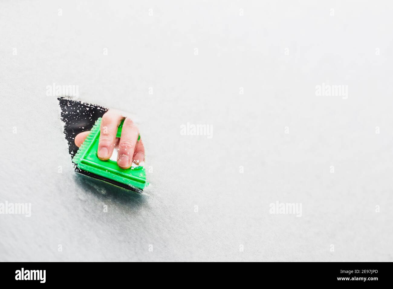 Une main avec un grattoir en plastique nettoie le pare-brise glace et neige en hiver - espace copie Banque D'Images