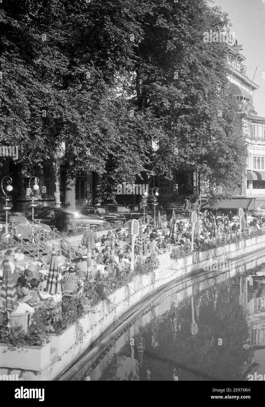 Photographie d'époque en noir et blanc des années 1950 montrant les rives de la Seine à Paris avec de nombreuses personnes appréciant dîner et boire dans les bars et cafés au bord de la rivière. Au loin à droite, on peut voir le Lido Building. Banque D'Images