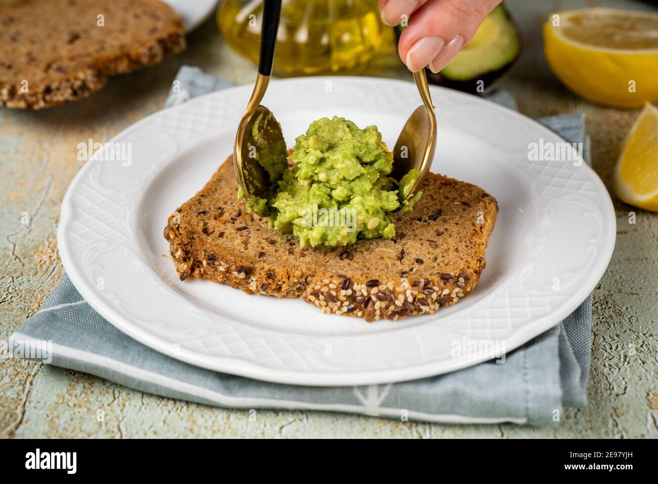 Mettre de l'avocat écrasé sur une tranche de pain sain par deux cuillères Banque D'Images