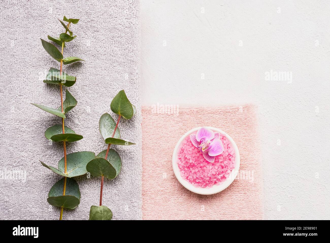 Serviettes roulées, sel de bain rose et branche d'eucalyptus sur fond de béton blanc. SPA, hygiène, bien-être bien-être, concept de soins du corps. Espace de copie, fl Banque D'Images