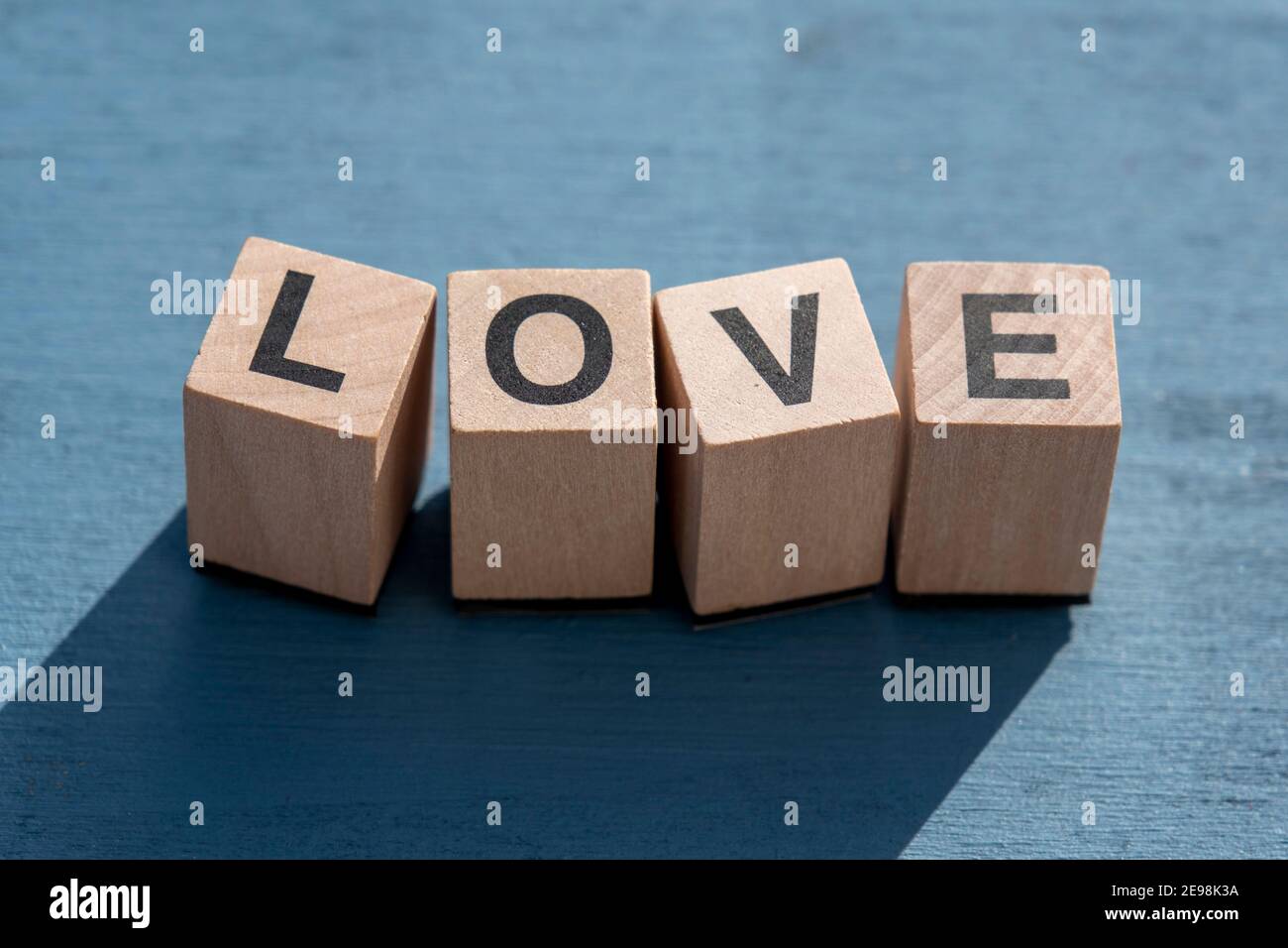 Le concept du jour et de l'émotion heureuse de Valentin : le mot AMOUR écrit avec des lettres cubes en bois simples faites pour les jeux de société sur une surface texturée bleue. Banque D'Images
