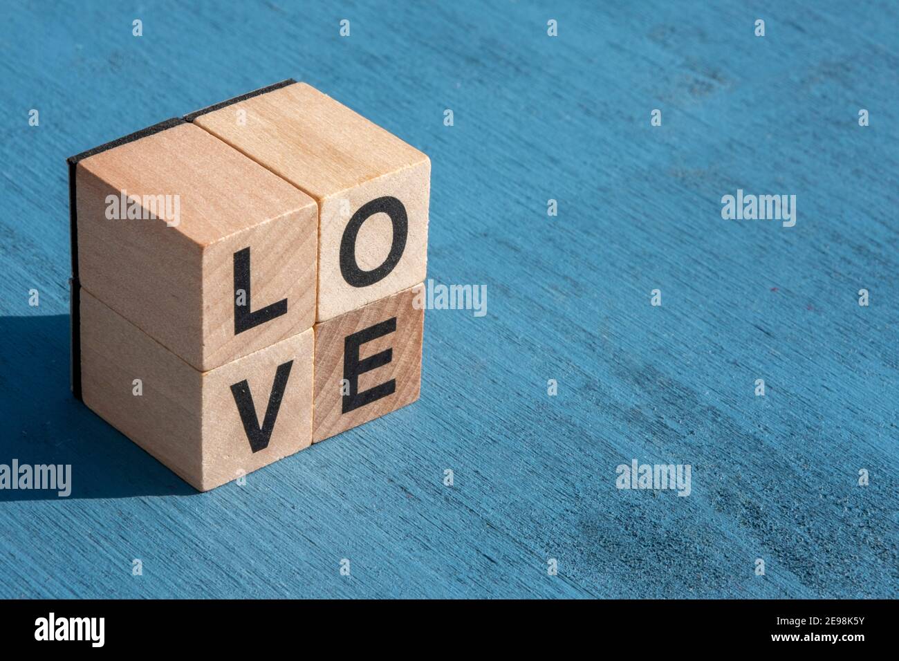 Le concept du jour et de l'émotion heureuse de Valentin : à gauche, le mot AMOUR écrit avec des lettres cubes en bois simples faites pour les jeux de société sur une surface texturée bleue Banque D'Images