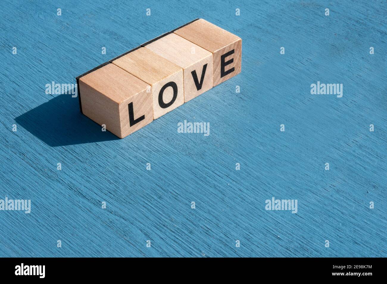 Le concept du jour et de l'émotion heureuse de Valentin : à gauche, le mot AMOUR écrit avec des lettres cubes en bois simples faites pour les jeux de société sur une surface texturée bleue Banque D'Images