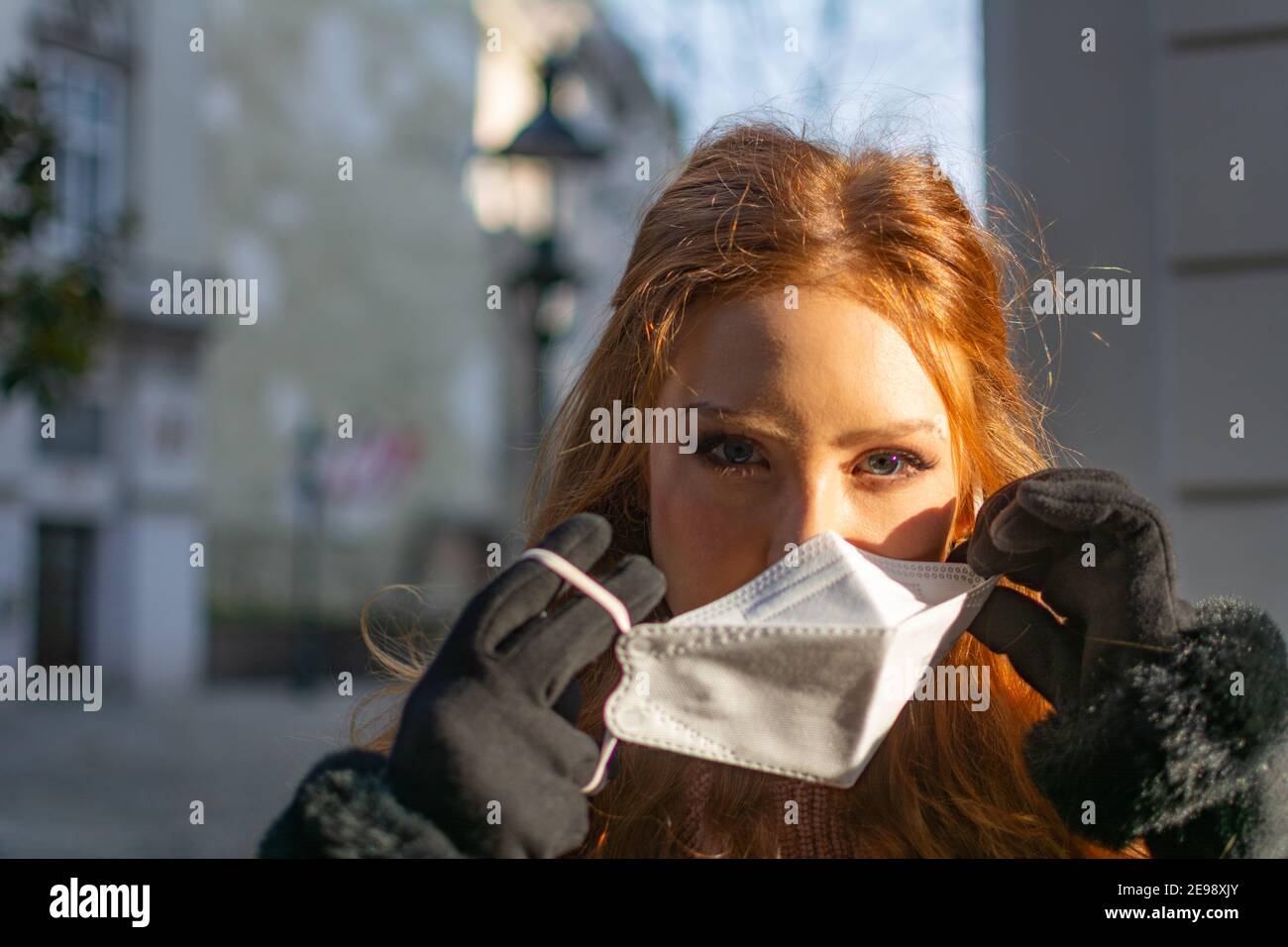 Bonne jeune femme avec les yeux bleus et les cheveux de gingembre en retrait Un masque protecteur pour le visage (FFP-2) pendant la pandémie de COVD-19 Banque D'Images