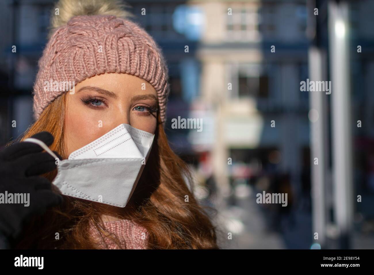 Bonne jeune femme avec les yeux bleus et les cheveux de gingembre en retrait Un masque protecteur pour le visage (FFP-2) pendant la pandémie de COVD-19 Banque D'Images