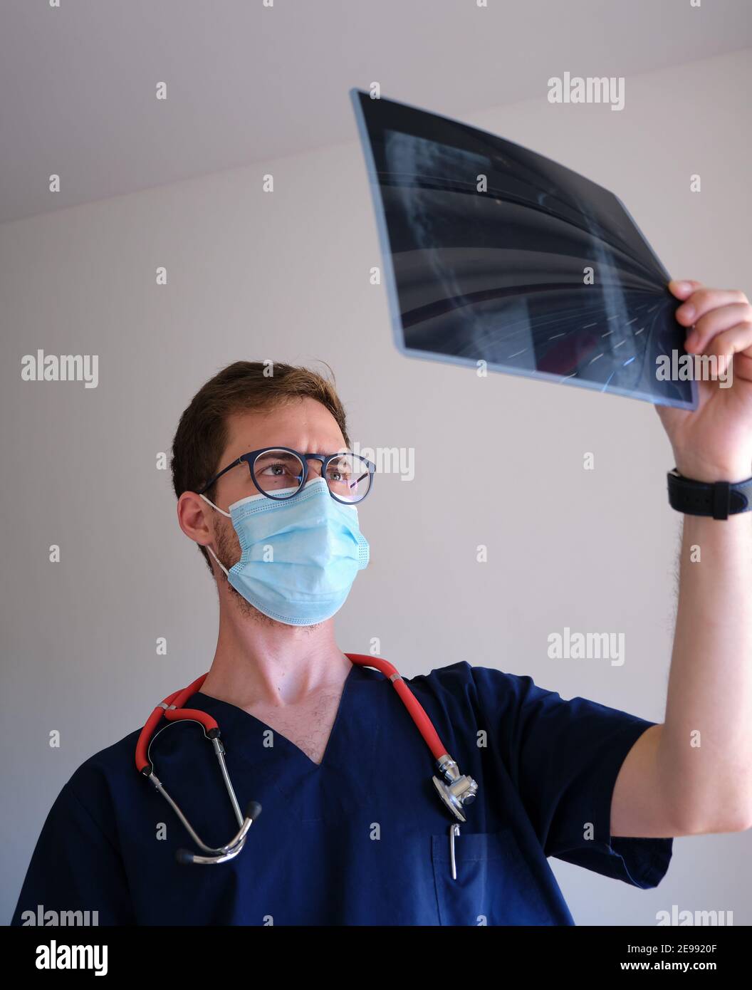 un beau médecin qui porte un gommage, un stéthoscope et un masque facial regardant une radiographie pendant la pandémie du cov 2 du sras Banque D'Images