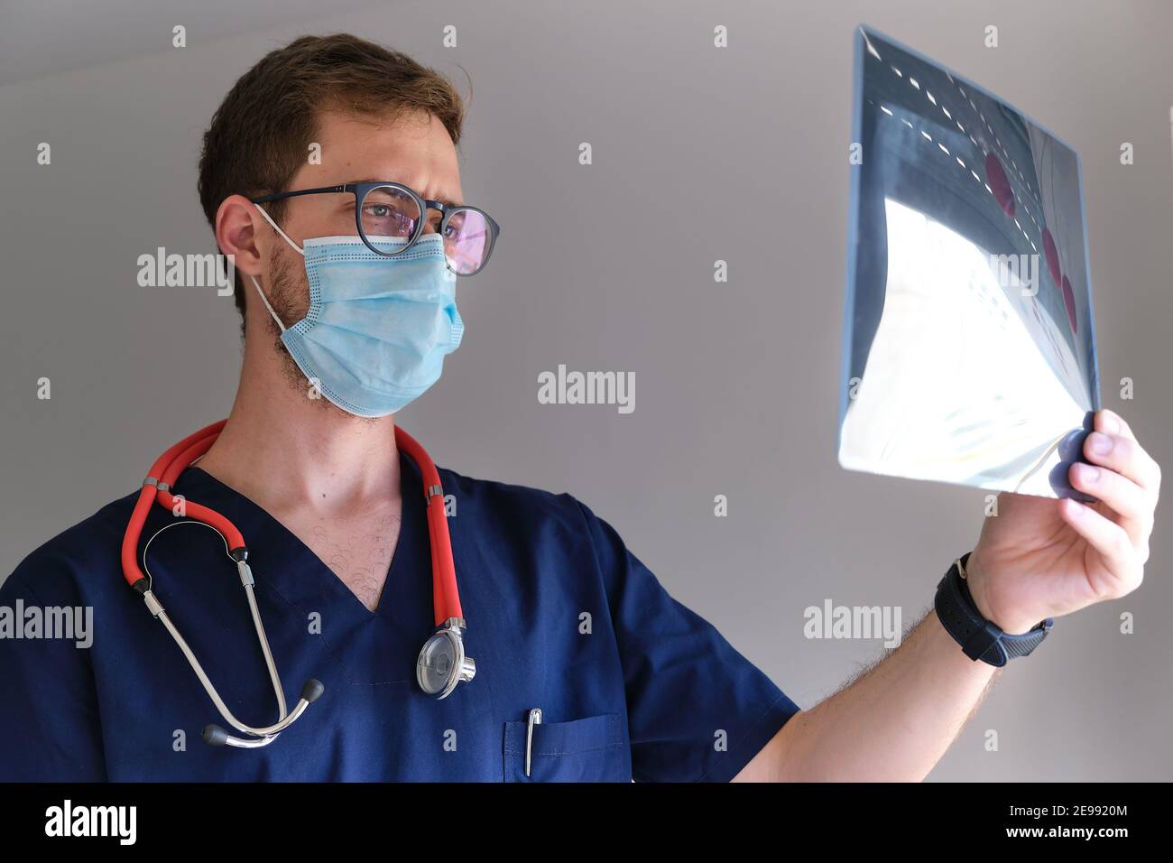 un beau médecin qui porte un gommage, un stéthoscope et un masque facial regardant une radiographie pendant la pandémie du cov 2 du sras Banque D'Images