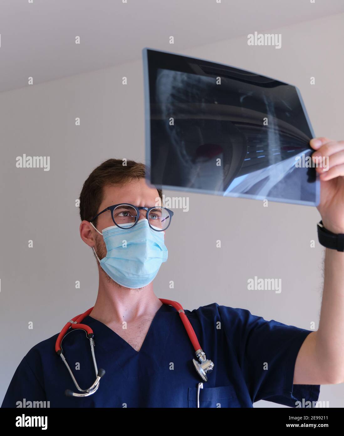 un beau médecin qui porte un gommage, un stéthoscope et un masque facial regardant une radiographie pendant la pandémie du cov 2 du sras Banque D'Images