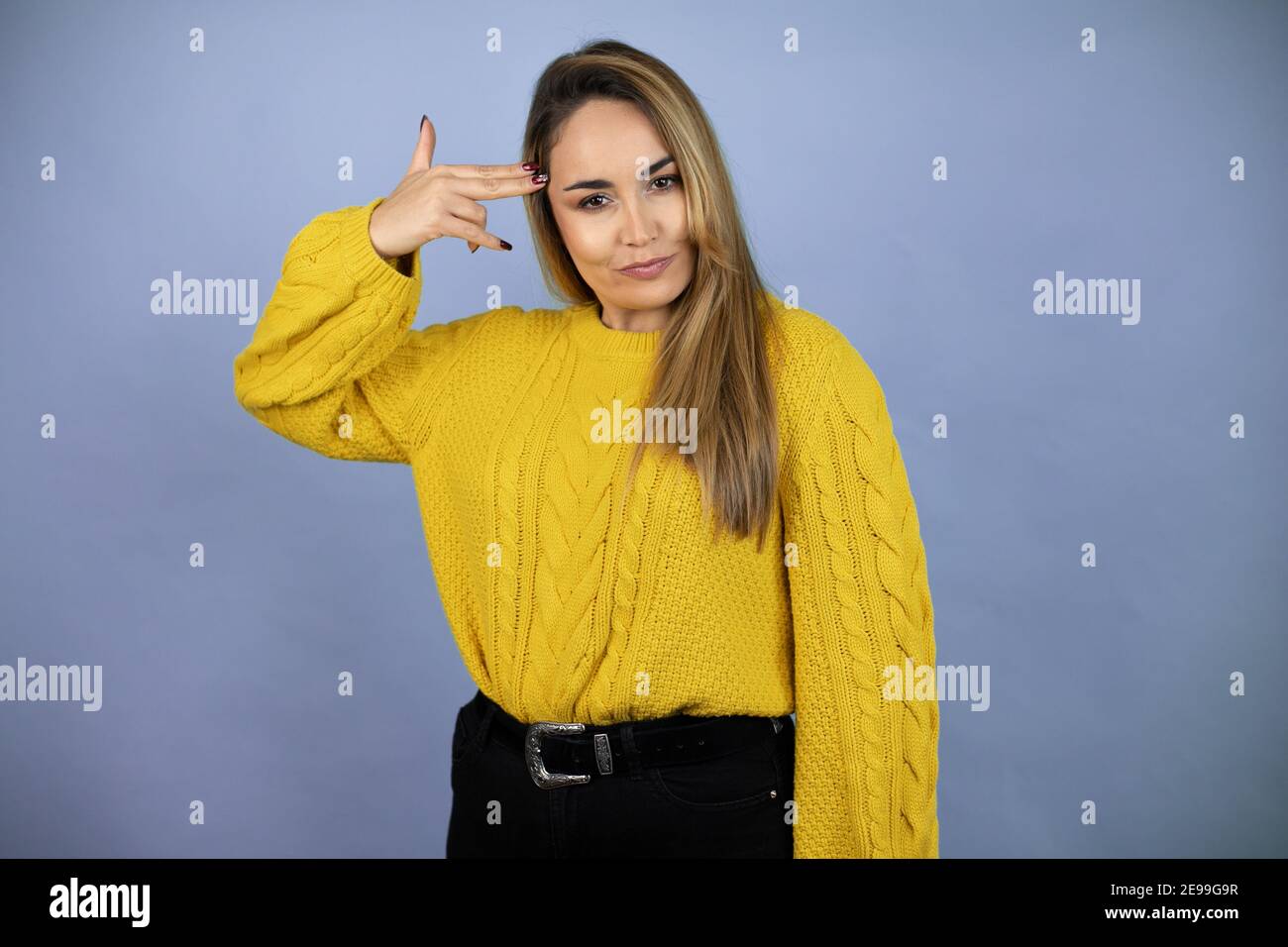 Jeune belle femme blonde avec de longs cheveux portant un chandail jaune de tir et de se tuer pointant la main et les doigts à la tête comme un fusil, suicide Banque D'Images