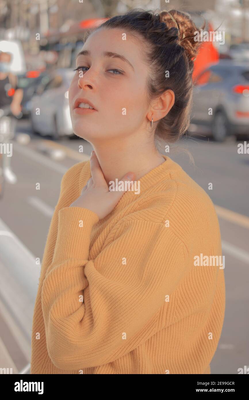 Portrait jeune femme avec chandail jaune dans un centre-ville plein de plusieurs voitures en circulation sur la route par une journée ensoleillée. Photographie de printemps 2021. Banque D'Images