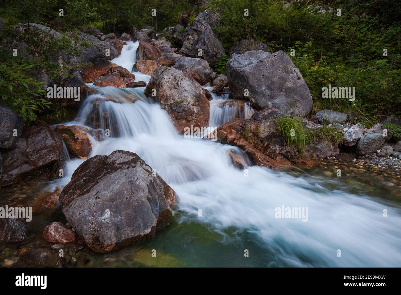 Un beau ruisseau de montagne des Alpes carniques avec de l'eau verte bleu clair et glacée entourée de grands rochers. Banque D'Images