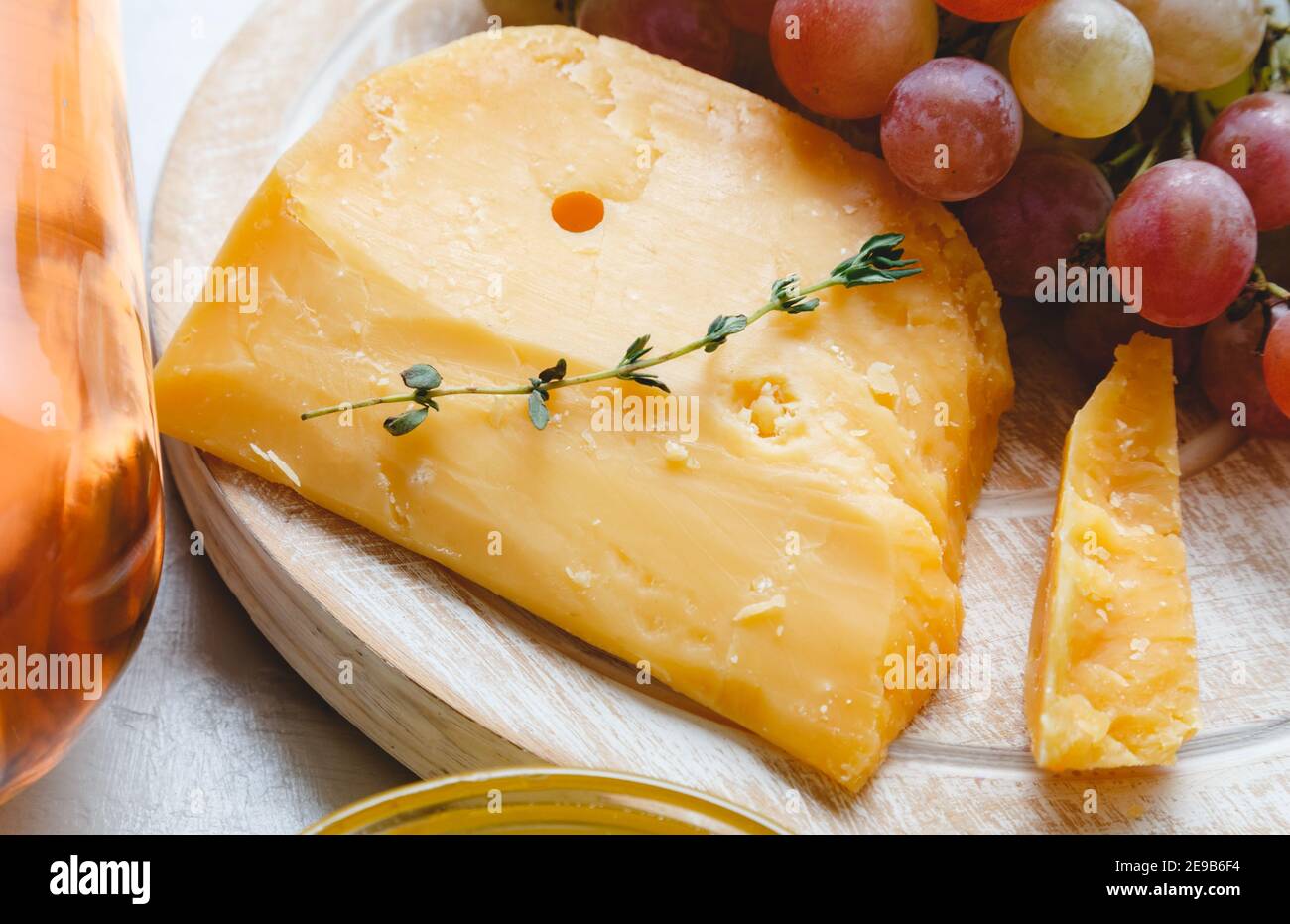 Cheddar aux raisins, vin rose, miel. En-cas au vin et au fromage pour un dîner romantique. Fromage gouda hollandais vieilli sur la planche à fromage avec des herbes de cumin Banque D'Images