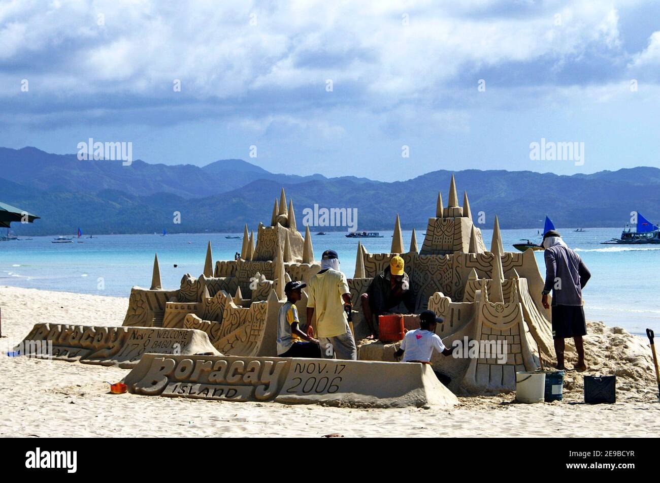 Les gens travaillent sur un château de sable élaboré sur White Beach à Boracay, aux Philippines. Le château de sable est juxtaposé aux collines lointaines et aux eaux bleues au large de l'île Boracay. Banque D'Images