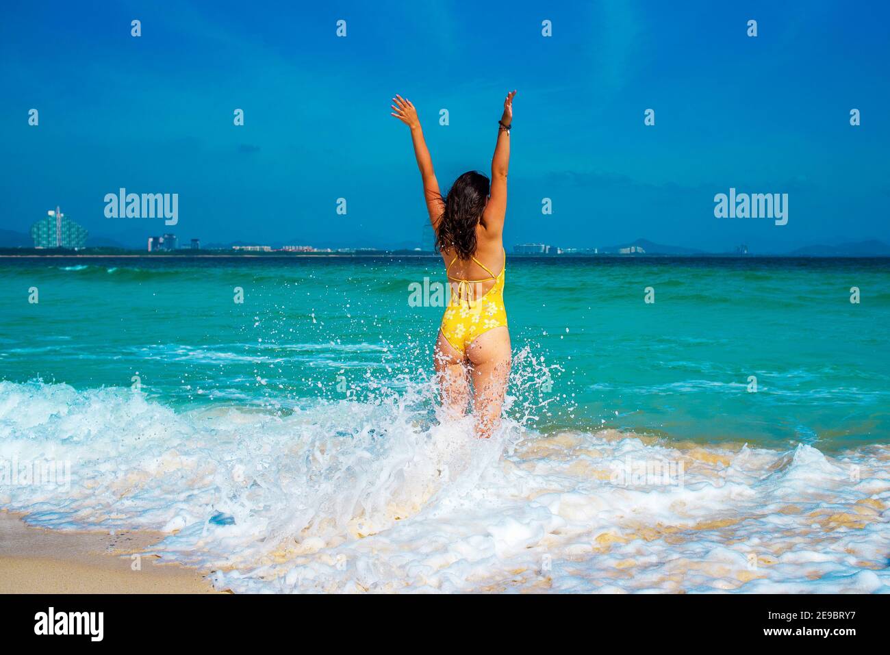 Jeune fille en maillot de bain jaune bondit joyeusement sur les vagues dans  la mer. Magnifique mer azur et ciel bleu sur fond. Hainan Paradise Island,  ville de Sanya Photo Stock -