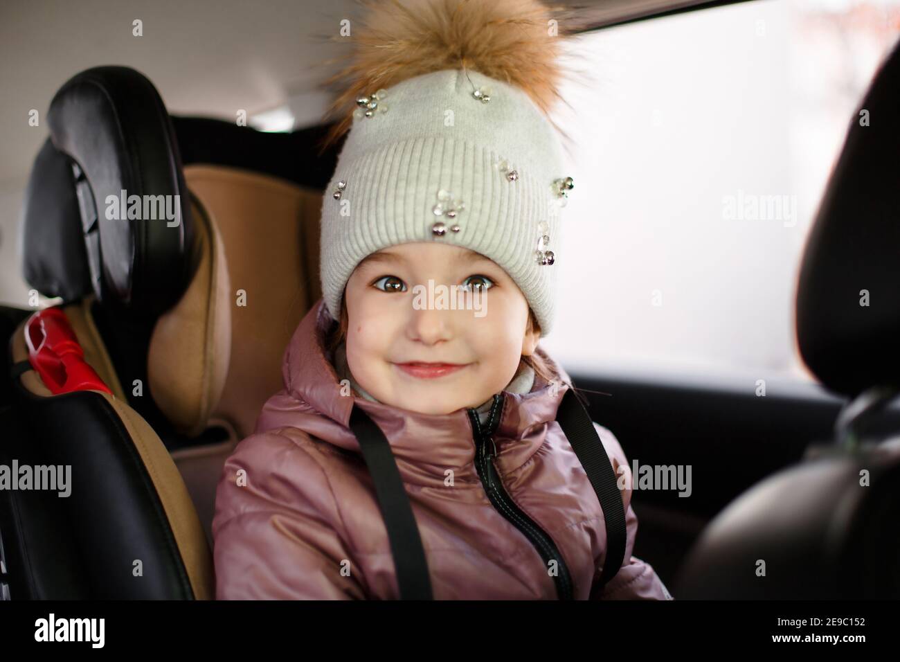 La jeune fille est assise dans le siège d'un enfant, portant des ceintures de sécurité. Sécurité routière, transport des enfants à l'intérieur de la voiture. Un enfant dans un chapeau avec un po Banque D'Images