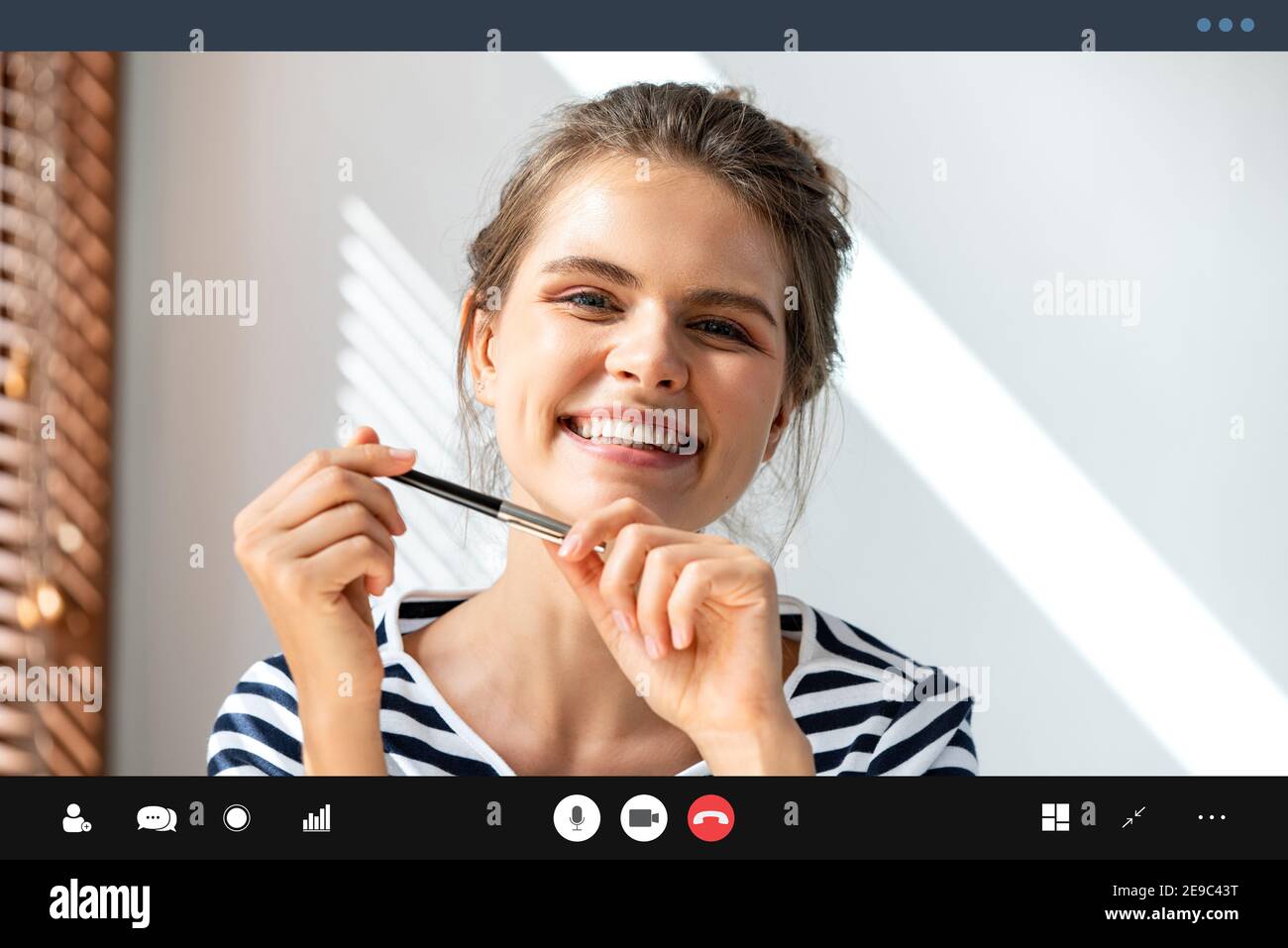 Femme caucasienne souriante tenant un stylo et regardant la caméra tout en effectuant des appels de vidéo conférence dans le salon, apprenant et travaillant à domicile concept Banque D'Images