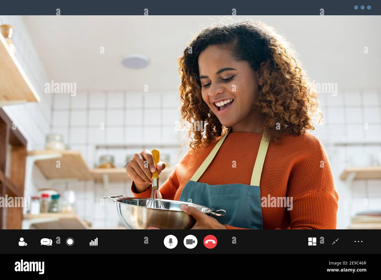 Jeune femme afro-américaine heureuse qui fait un appel vidéo tout en cuisinant dans la cuisine à la maison pendant le temps libre Banque D'Images