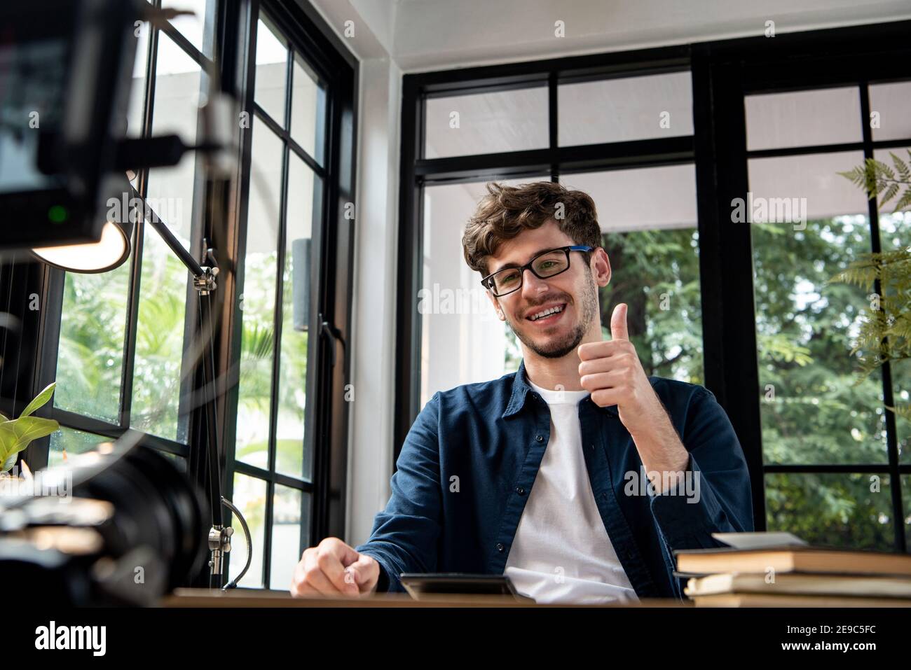 Souriant homme caucasien vlogger donner des pouces vers le haut tout en enregistrant la vidéo clip avec carmera à la maison pour le partager sur les réseaux sociaux Banque D'Images