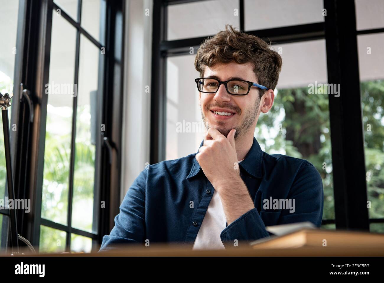 Homme caucasien souriant assis dans un café et pensant à la main sur le menton Banque D'Images