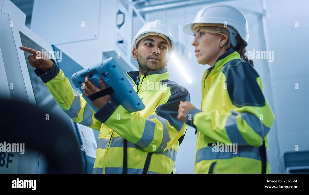 Ingénieur en chef et chef de projet portant des gilets de sécurité et des chapeaux durs, utilisez le contrôleur de tablette numérique dans Modern Factory, Talking, Programming machine Banque D'Images