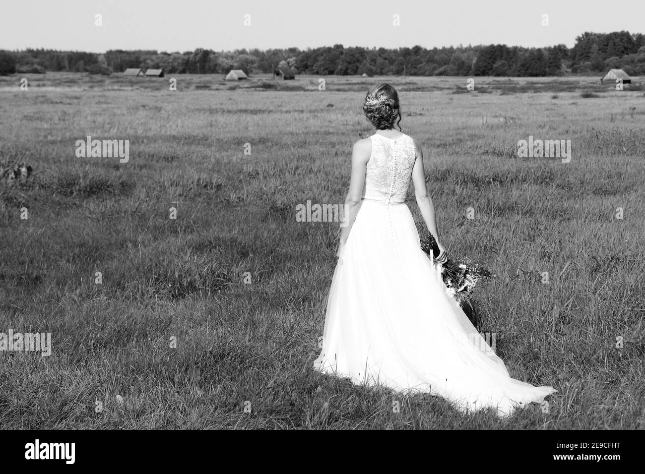 Une mariée est debout sur la prairie et regarde de rêve loin. Elle tient le bouquet de fleurs dans sa main. Banque D'Images
