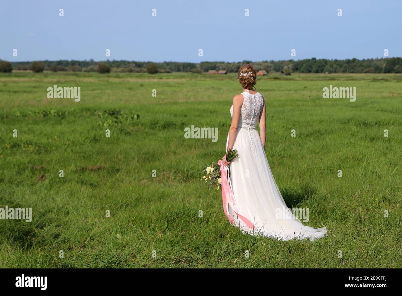 Une mariée est debout sur la prairie et regarde de rêve loin. Elle tient le bouquet de fleurs dans sa main. Banque D'Images
