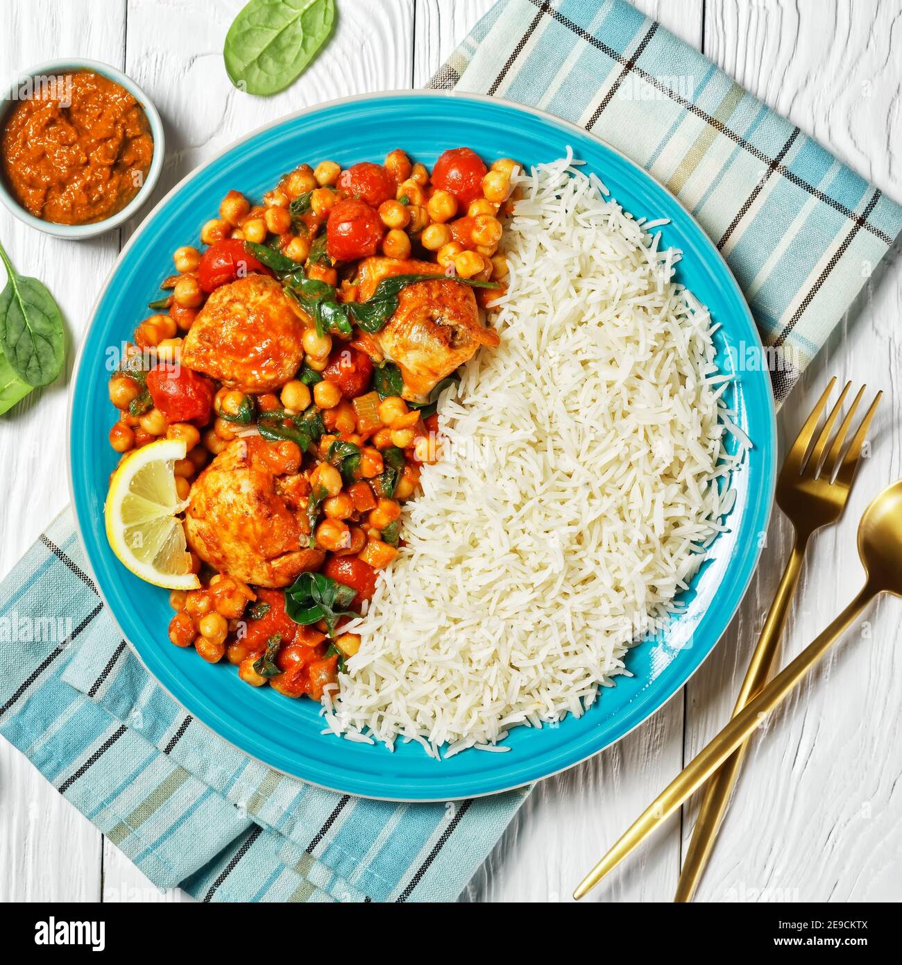 Poulet et curry de pois chiches avec riz aux tomates cerises, épinards, gingembre, pâte de curry jaune servie avec un coin de citron sur une assiette bleue sur un blanc Banque D'Images