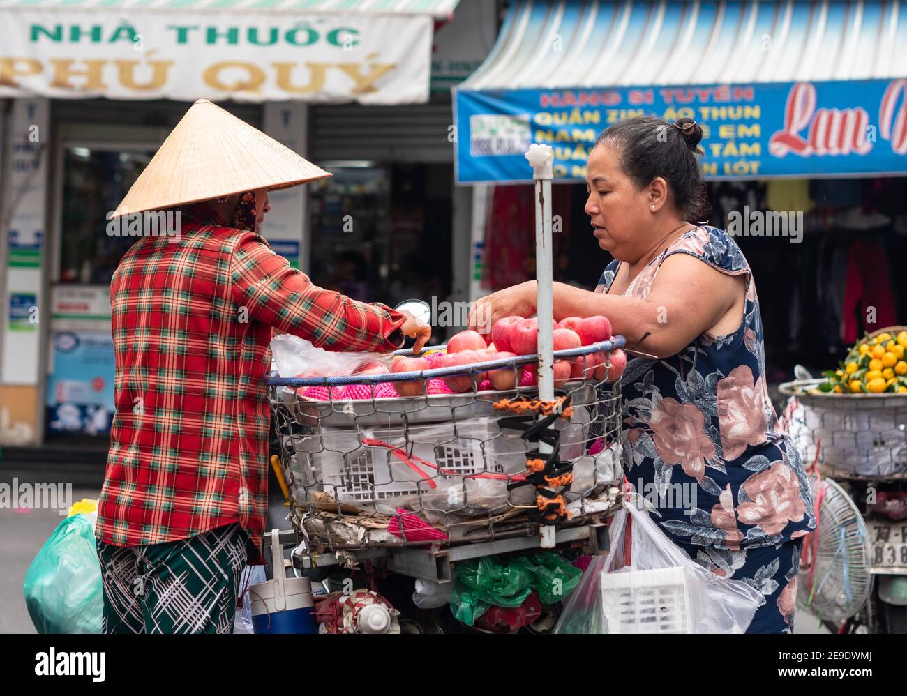 Vendeur de rue femelle vendant des pommes à une femme d'un panier sur son vélo à Ho Chi Minh ville, Vietnam. Banque D'Images