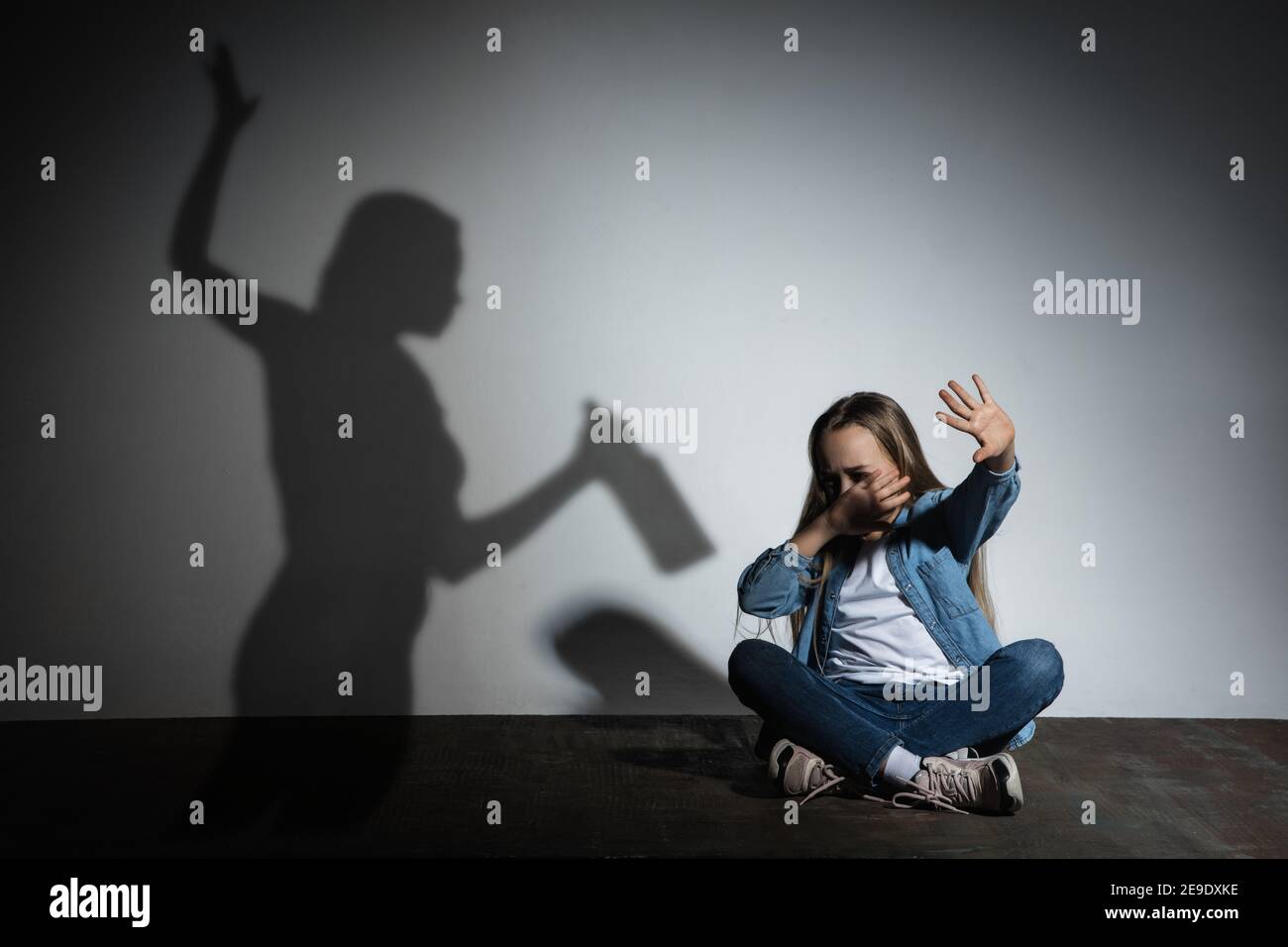 Violence physique domestique, abus. Petite fille caucasienne effrayée, victime assise près du mur blanc avec l'ombre de la mère en colère menaçant avec la dépendance à l'alcool. Sensibilisation au problème social. Banque D'Images