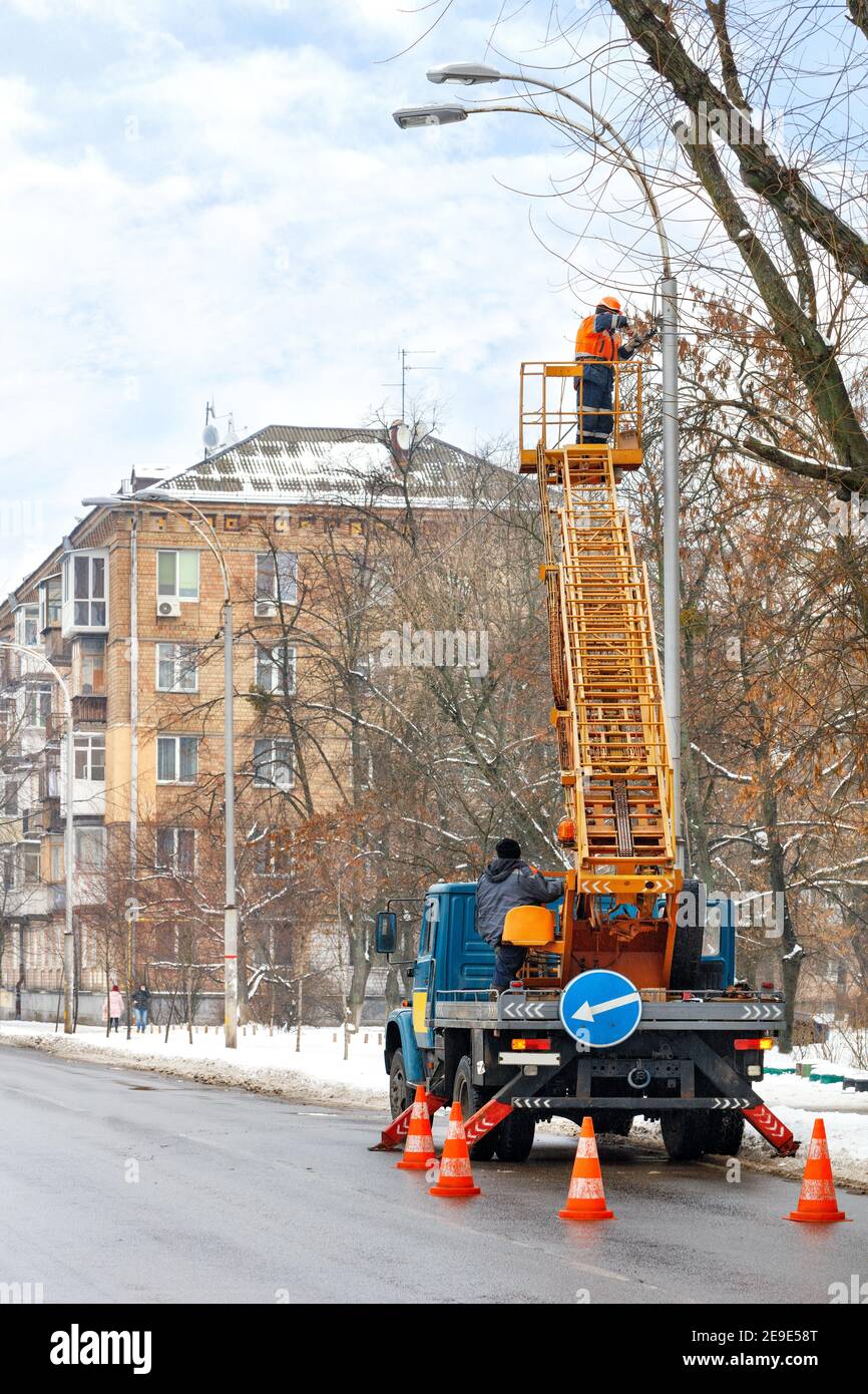 Les travailleurs de l'entretien routier d'un camion équipé d'une échelle télescopique vérifient le fonctionnement de l'éclairage de la rue en hiver. Espace de copie, image verticale. Banque D'Images