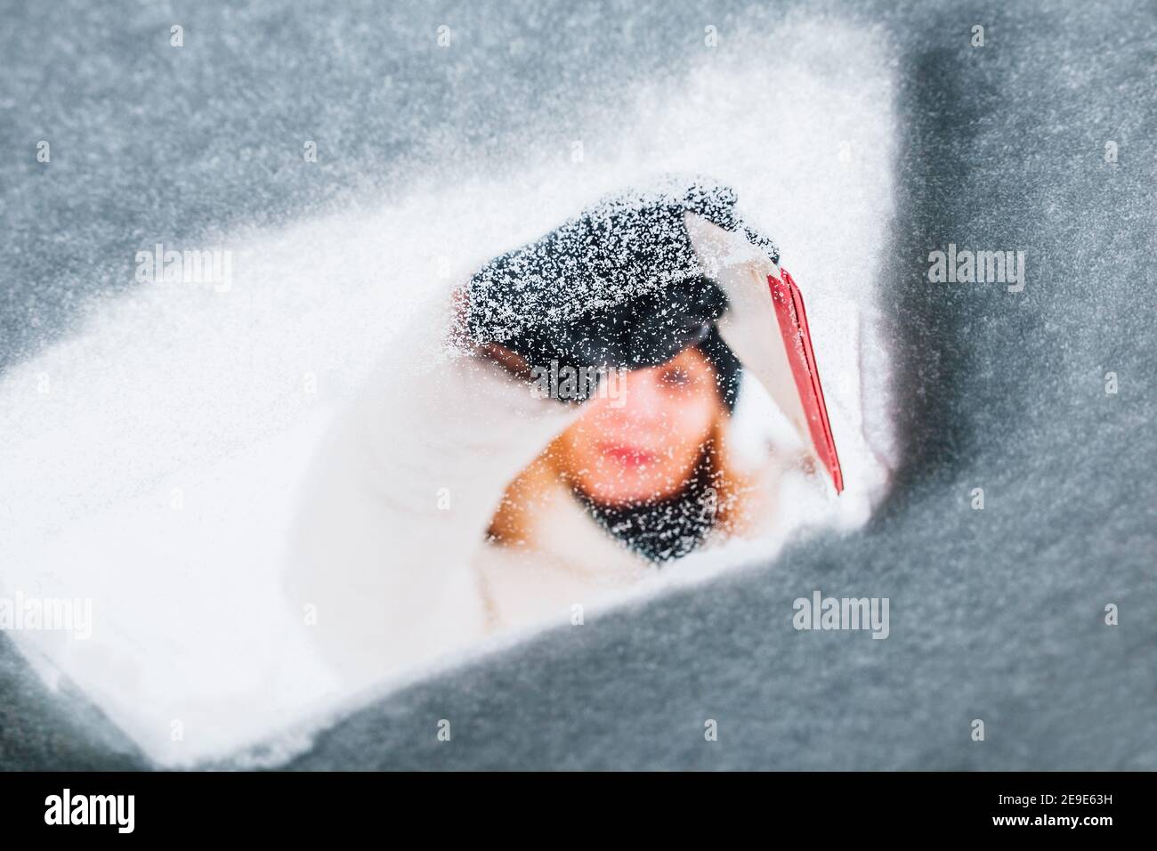 Femme en hiver pour nettoyer la voiture de la neige elle lui-même - elle brosse le pare-brise recouvert de neige Banque D'Images