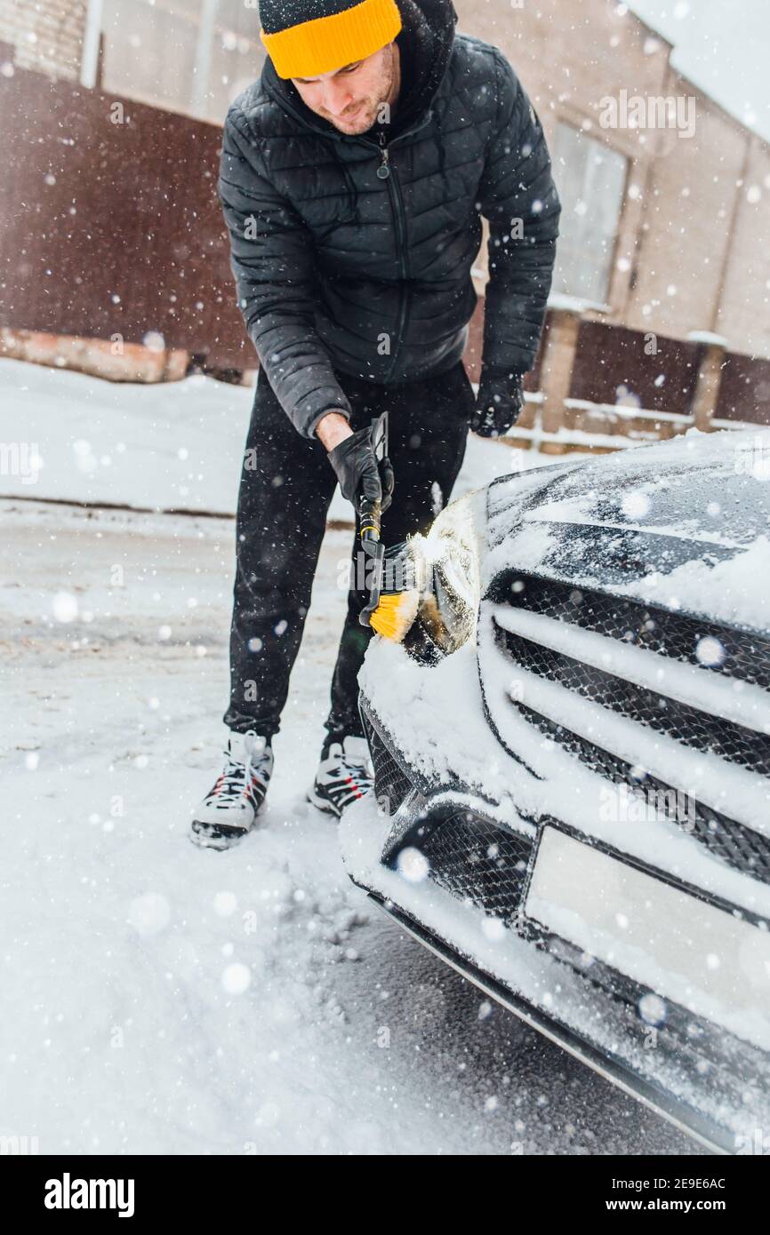 Un homme avec une brosse pour nettoyer les phares de une voiture de neige et de glace - temps d'hiver Banque D'Images