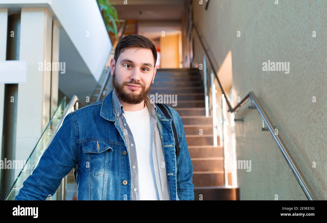 Étudiant sur les escaliers bruns. Portrait d'un jeune homme confiant, d'un beau homme à barbe caucasien avec sac à dos dans le couloir du campus universitaire de réouverture. Indépendant Banque D'Images