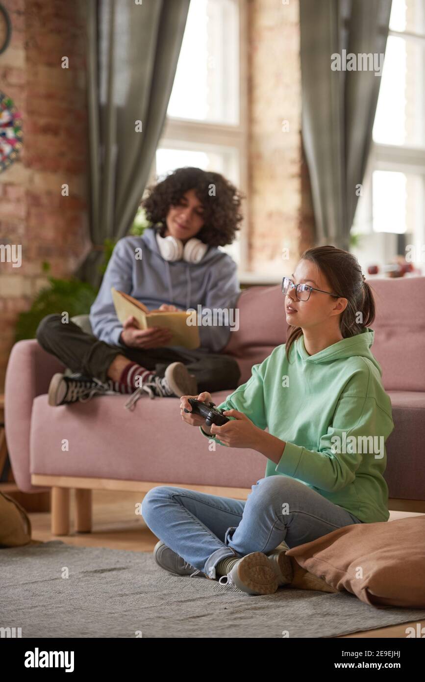 Deux adolescents se reposant à la maison jouant à des jeux vidéo et de lecture livres Banque D'Images