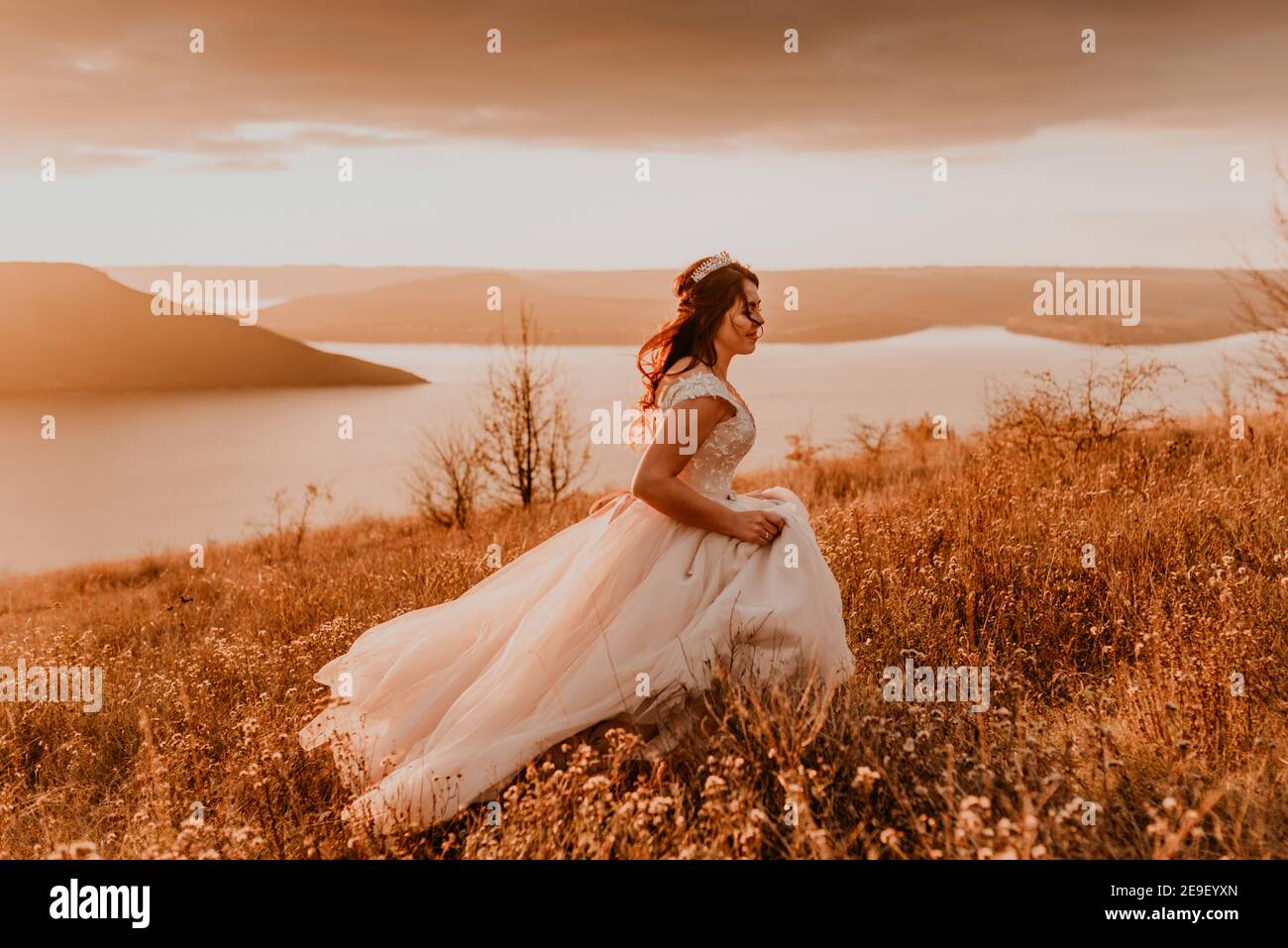 belle femme brune mariée en robe blanche et costume sont marcher sur de l'herbe haute dans le champ en été Banque D'Images