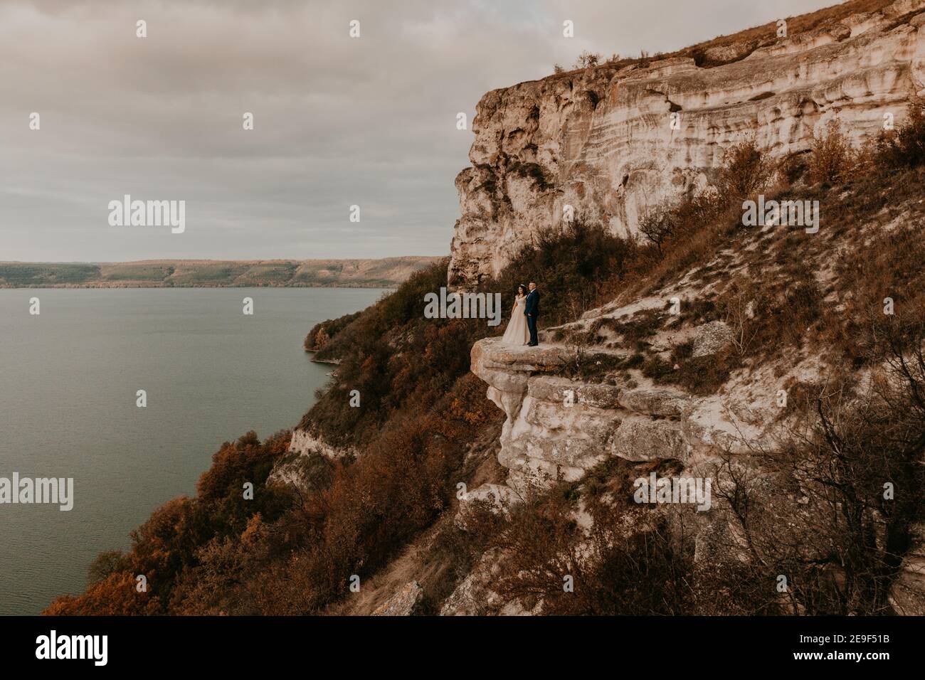 marié en costume et mariée dans un stand de robe sur une falaise de pierre au-dessus de la rivière. Montagne près du lac. Vue aérienne de drone. monastère de rock à bakota Banque D'Images