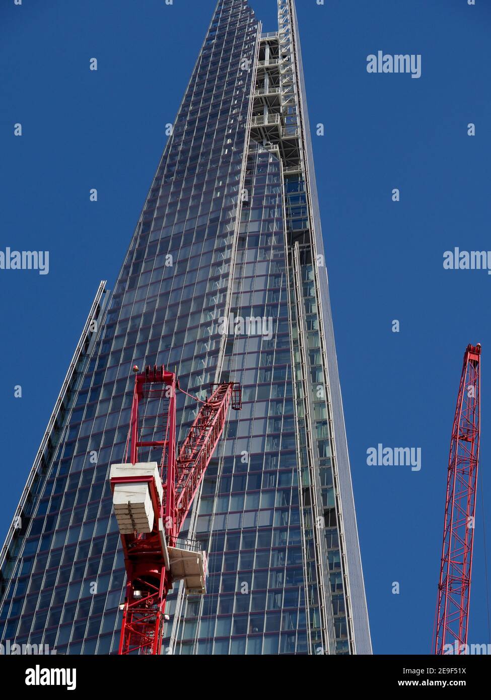 Vue sur le bâtiment Shard dans un ciel bleu profond avec des grues à tour rouges au premier plan Banque D'Images