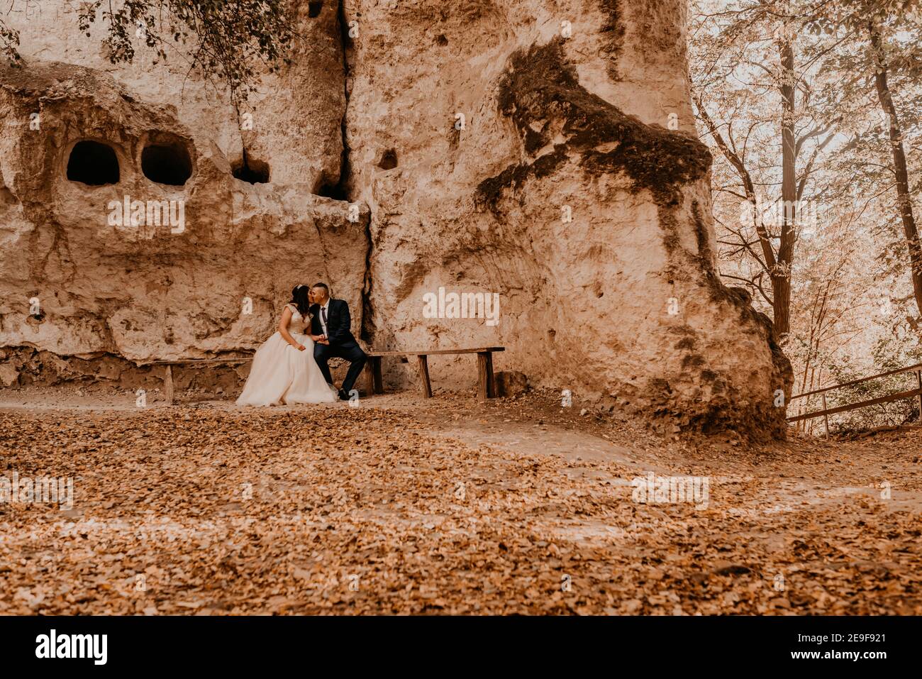 couple de mariage en amour homme et femme assis sur un banc sous le monastère de roche bakota dans la forêt d'automne sur fond de pierres. costume de marié et Banque D'Images