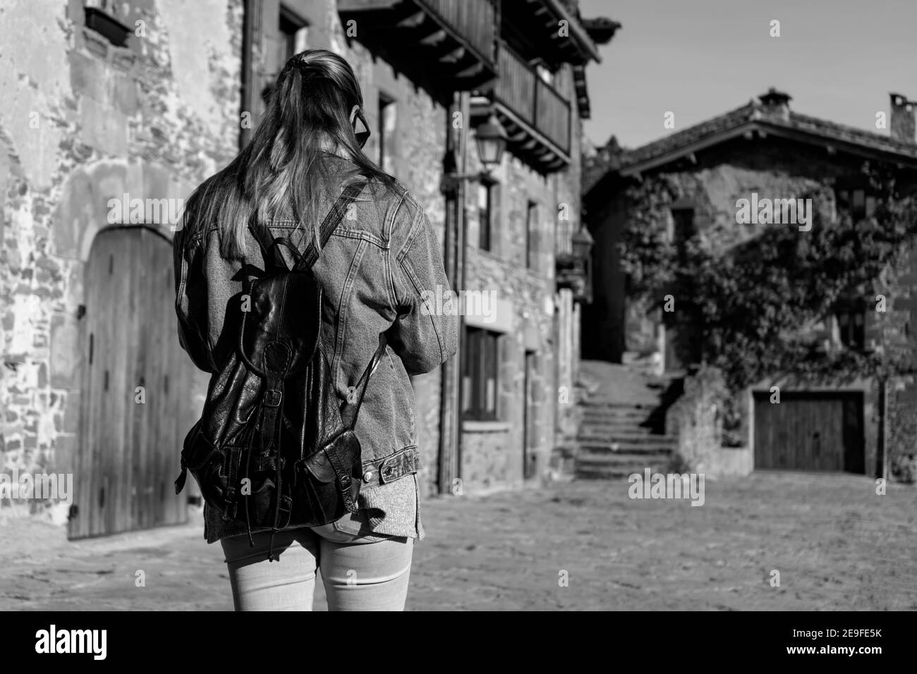 Jeune femme marchant avec jeans de mode veste et sac à dos dedans Vieux village médiéval.vue arrière, photographie en noir et blanc, voyage et concept du tourisme Banque D'Images