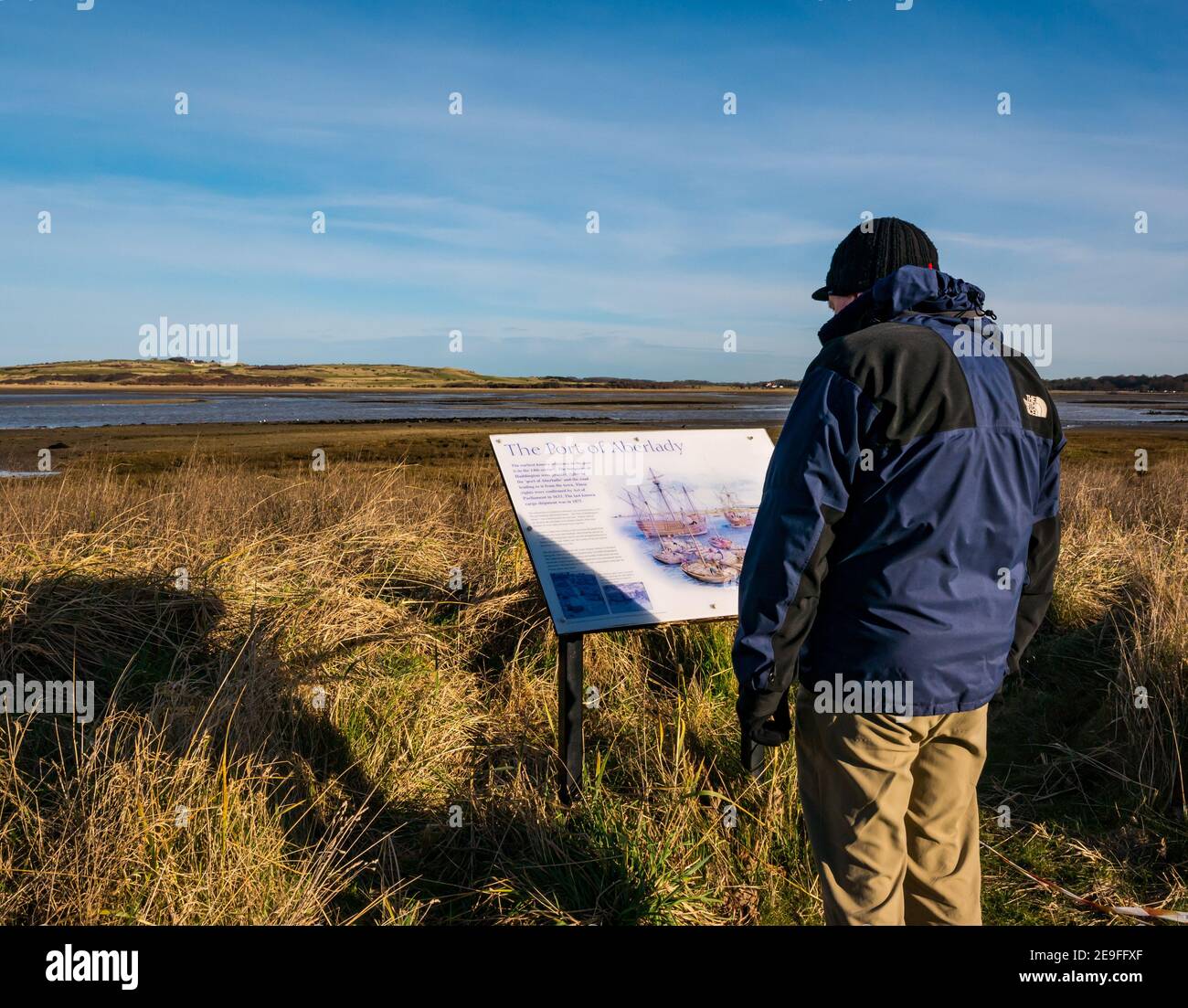 Homme regardant le panneau local d'information sur l'histoire maritime par temps froid ensoleillé, Réserve naturelle d'Aberlady Bay, East Lothian, Écosse, Royaume-Uni Banque D'Images