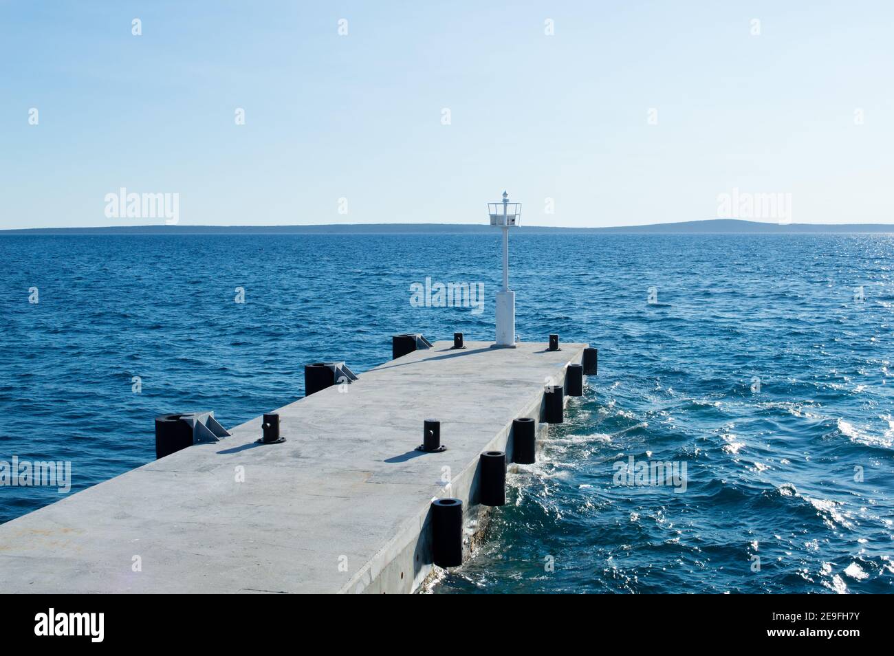 Quai en béton vide avec phare à signal blanc dans le port de l'île croate Silba, magnifique mer Adriatique bleue Banque D'Images