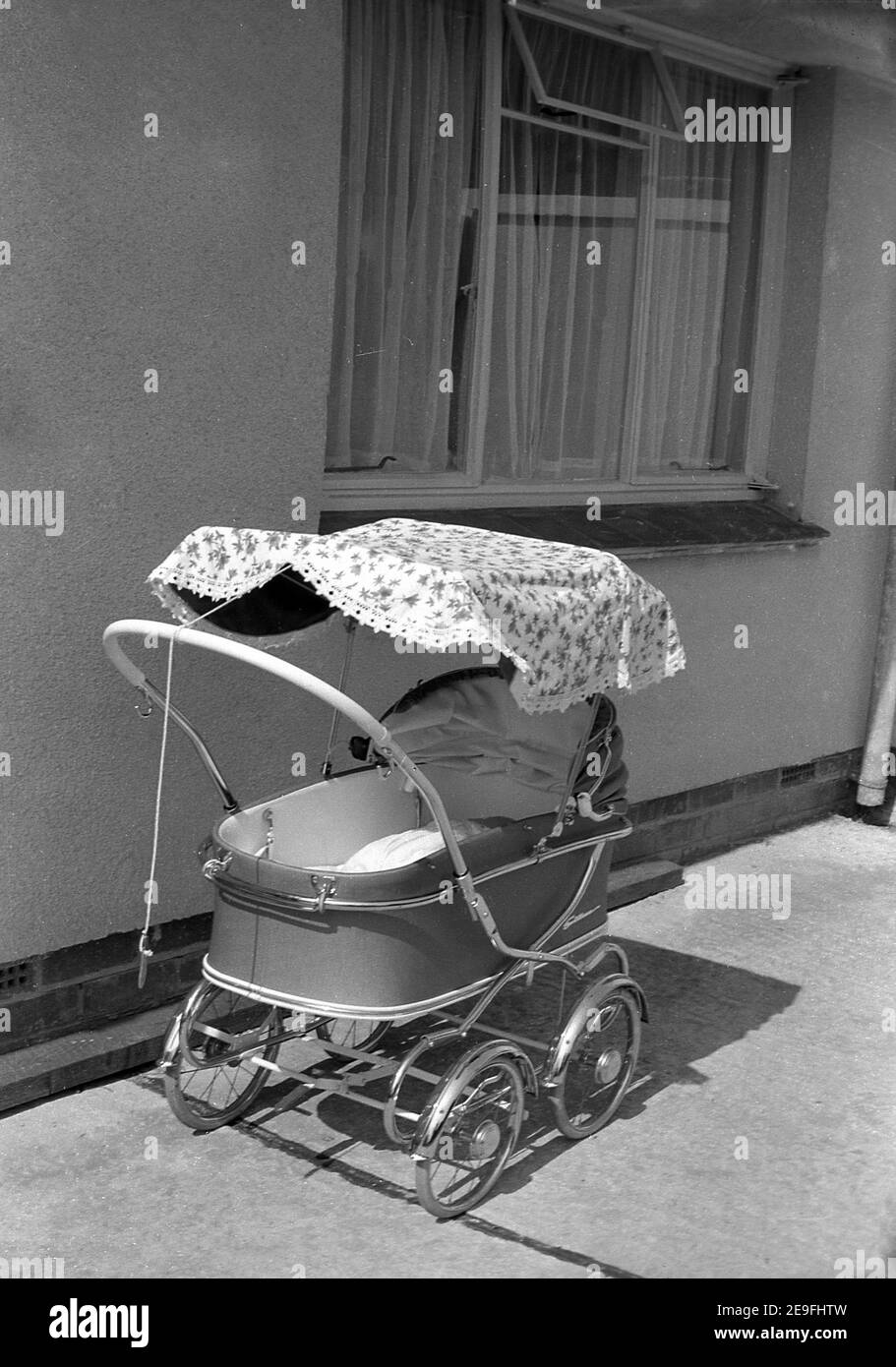 1963, pram historique, léger, à roues métalliques de l'époque avec capot à l'extérieur d'une maison, Angleterre, Royaume-Uni. Banque D'Images