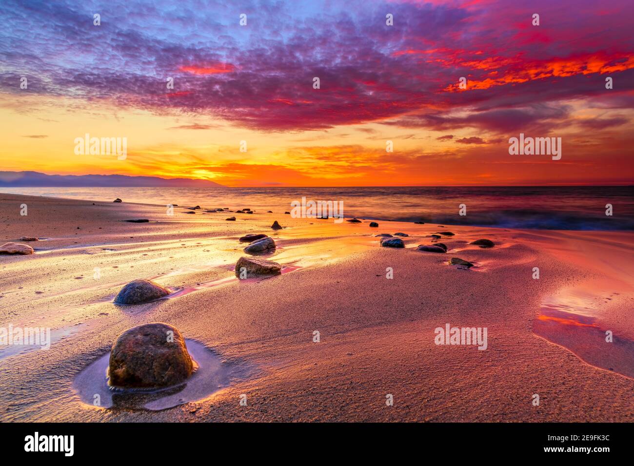 Un coucher de soleil coloré sur l'océan avec Rocks sur la plage et Un ciel de Cloudscape vibrant dans le ciel de coucher de soleil Banque D'Images