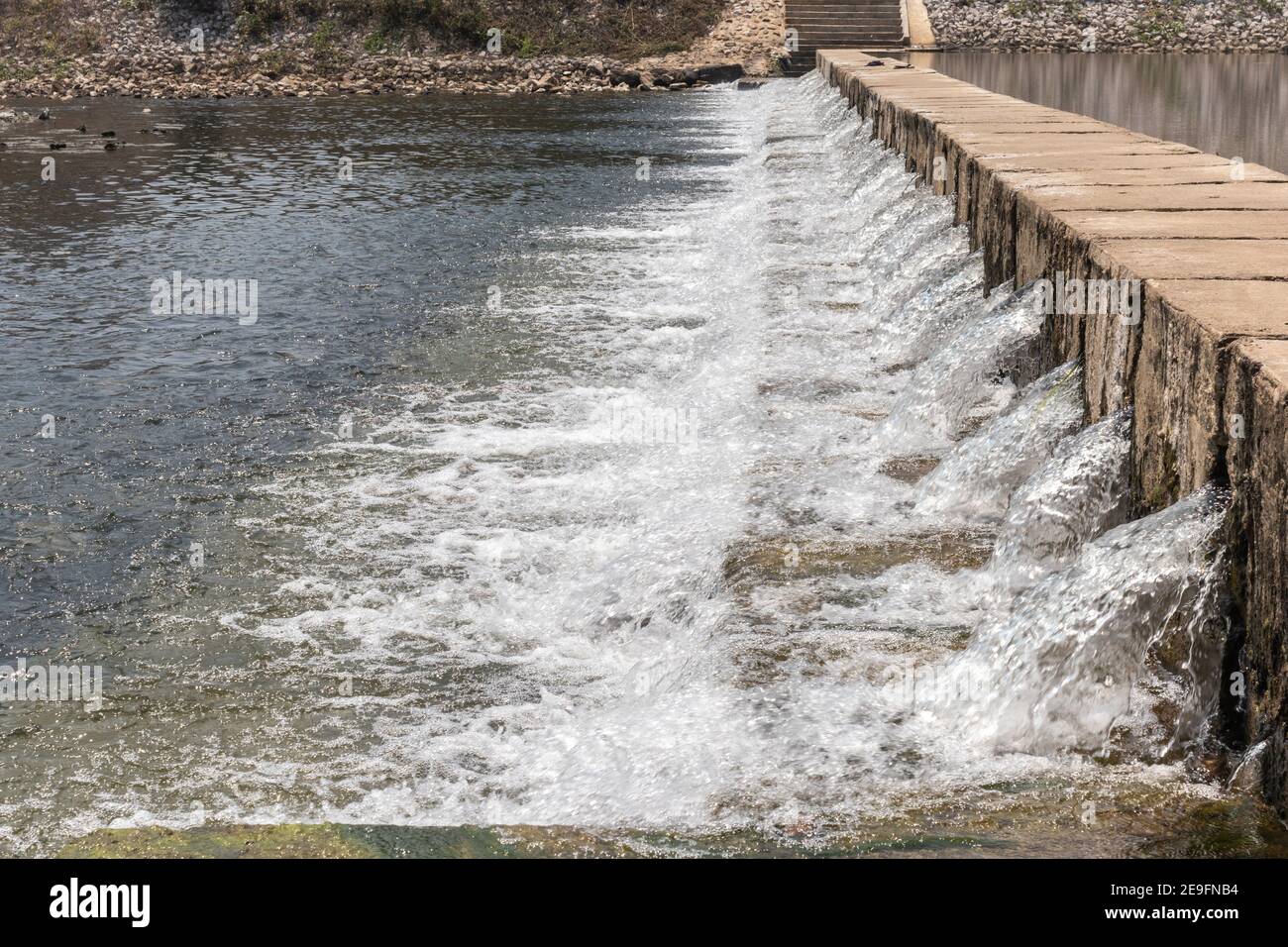 Le débit d'eau passe le déversoir du niveau supérieur au niveau inférieur du cours d'eau latéral de la rivière. Le déversoir forme une petite cascade. Banque D'Images