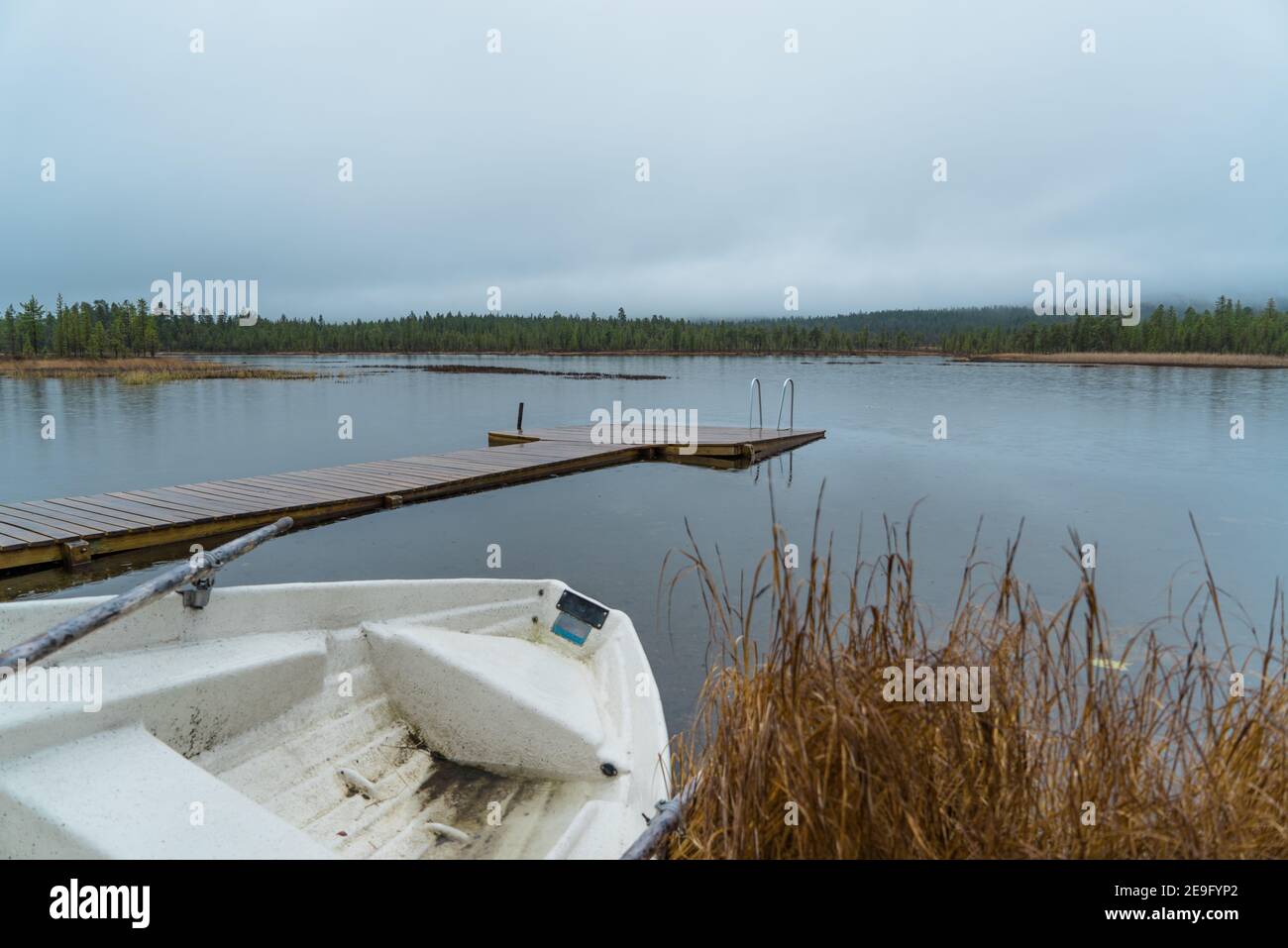 Vieux, sale, vieux bateau à ramer se trouvant à côté d'un petit lac d'arrivée typique à Inari, Finlande, Laponie. Jetée en bois dans une forêt pluvieuse paisible et relaxante Banque D'Images