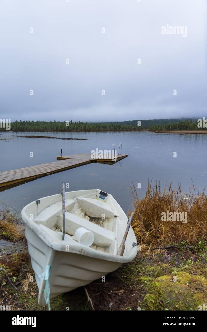 Vieux, sale, vieux bateau à ramer se trouvant à côté d'un petit lac d'arrivée à Inari, Finlande, Laponie. Jetée en bois à une journée tranquille et pluvieuse Banque D'Images