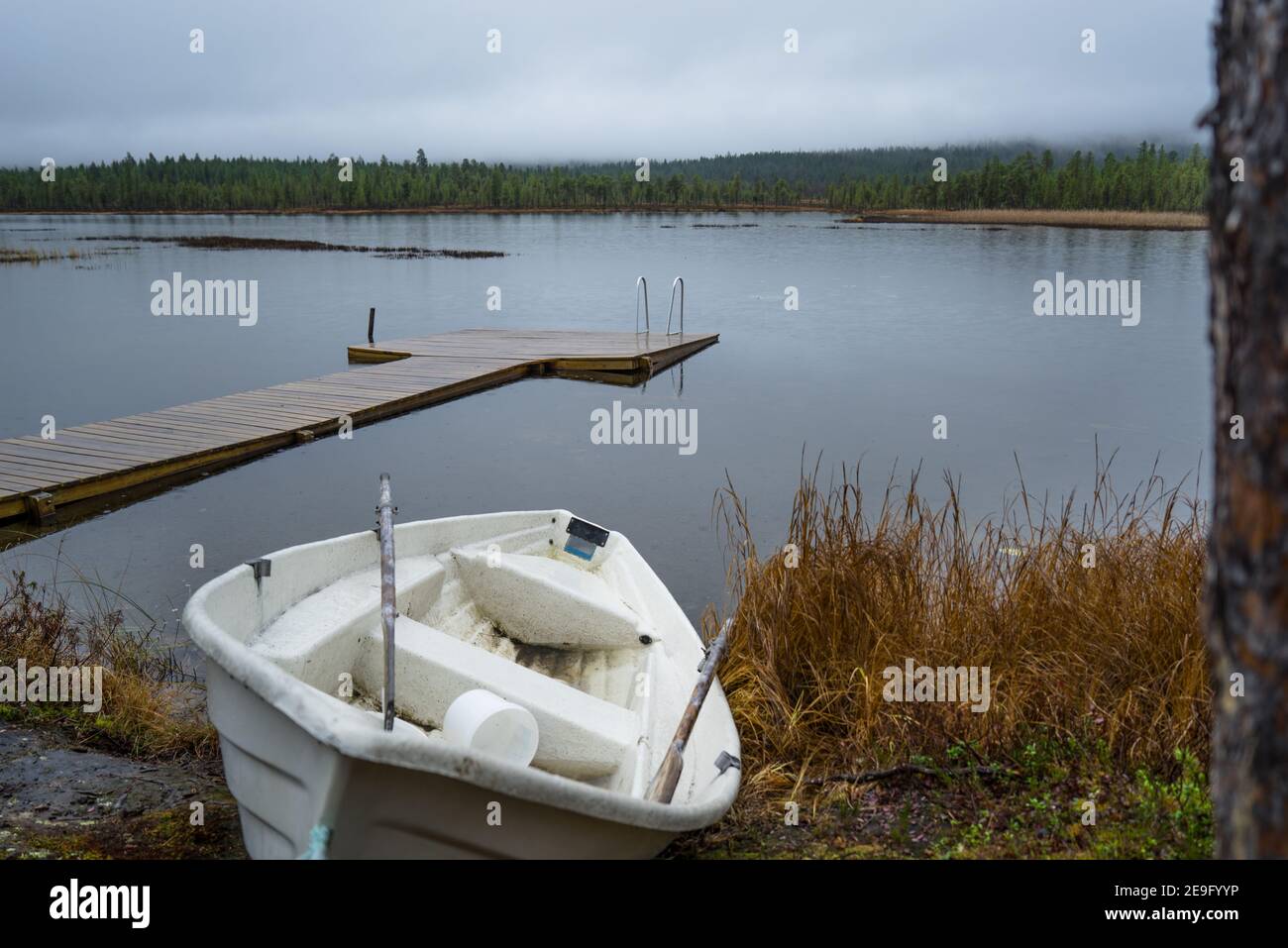 Ancien bateau à rames d'occasion se trouvant à côté d'un petit lac d'arrivée à Inari, en Finlande, en Laponie. Jetée en bois au cottage par une journée reposante, tranquille et pluvieuse Banque D'Images