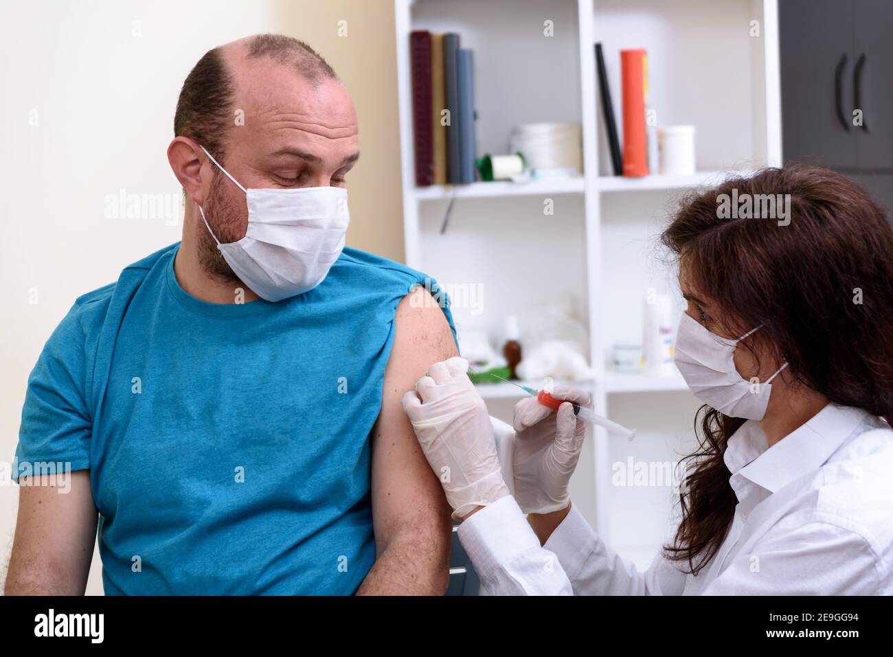 Médecin en gants tenant la seringue et faisant l'injection au patient dans le masque médical. Banque D'Images