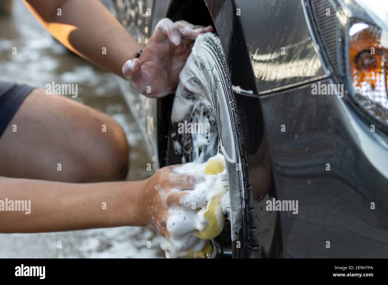 Laver à la main la roue de la voiture avec de l'eau savonneuse. L'homme nettoie la voiture avec une éponge, de l'eau et du détergent. Banque D'Images